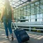 woman walking on pathway while strolling luggage