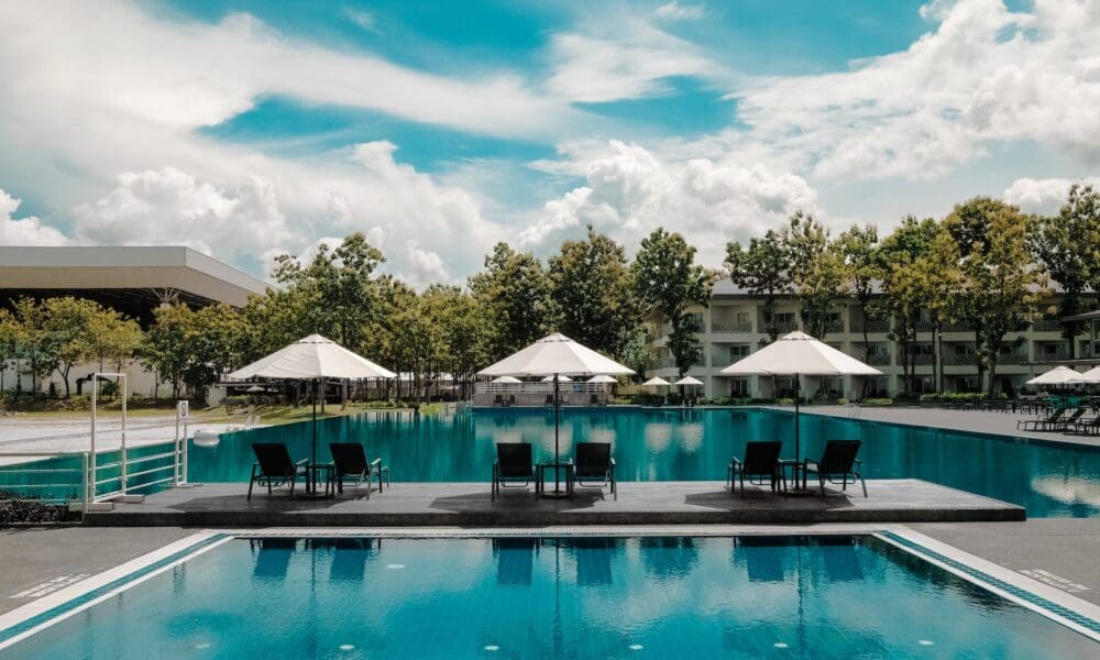 black outdoor lounge chair in between blue swimming pool under white cloudy blue sky