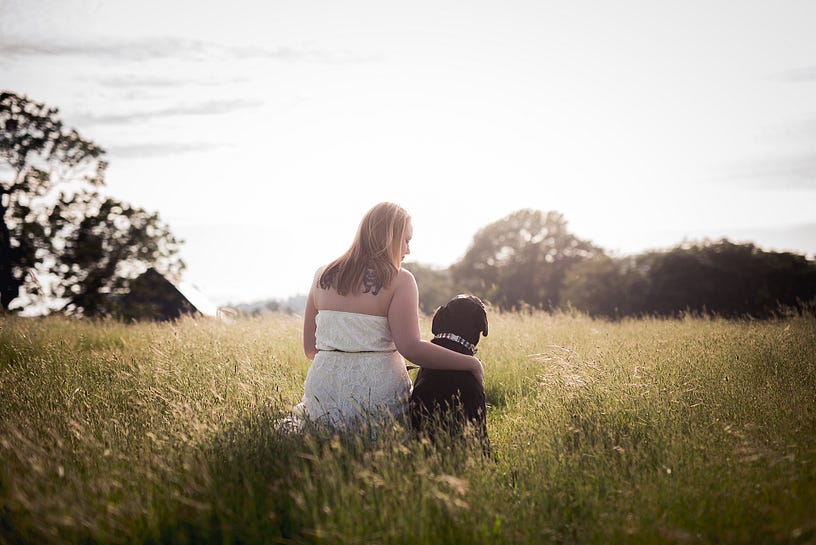 Woman and her dog staring off into the sunset. The dog is a black labrador retreiver.