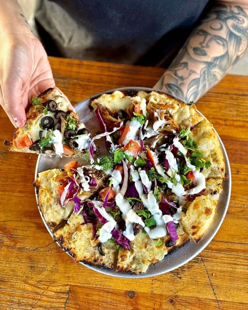 A hand picking up a slice of pizza from Backside Brewing Co in Roseburg, Oregon
